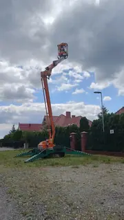 Podnośnik koszowy z wysięgnikiem uniesionym pionowo, kosz z operatorem ponad dachami domów